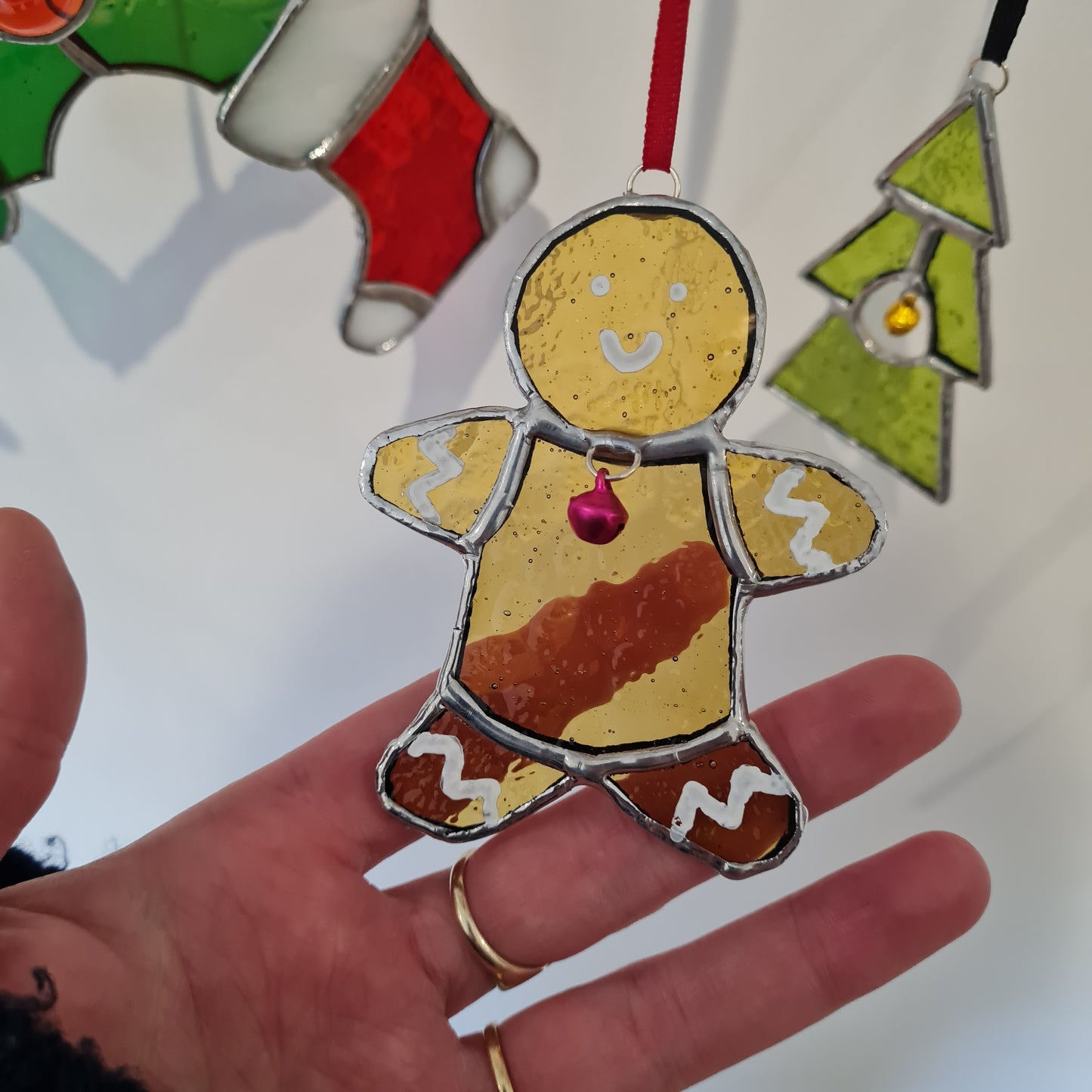 a staine glass ornament of a gingerbread man. amber muffled glass with white paint icing detail and a pink bell.