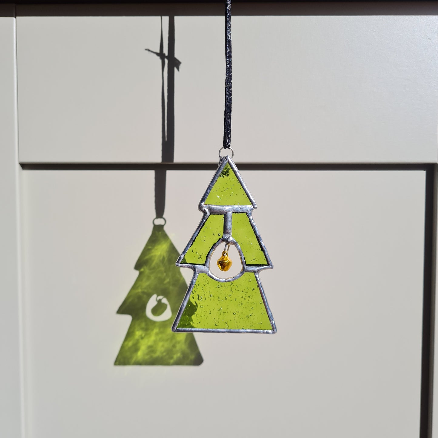 small stained glass Christmas tree, lime green glass and gold bell hanging in the middle of the tree