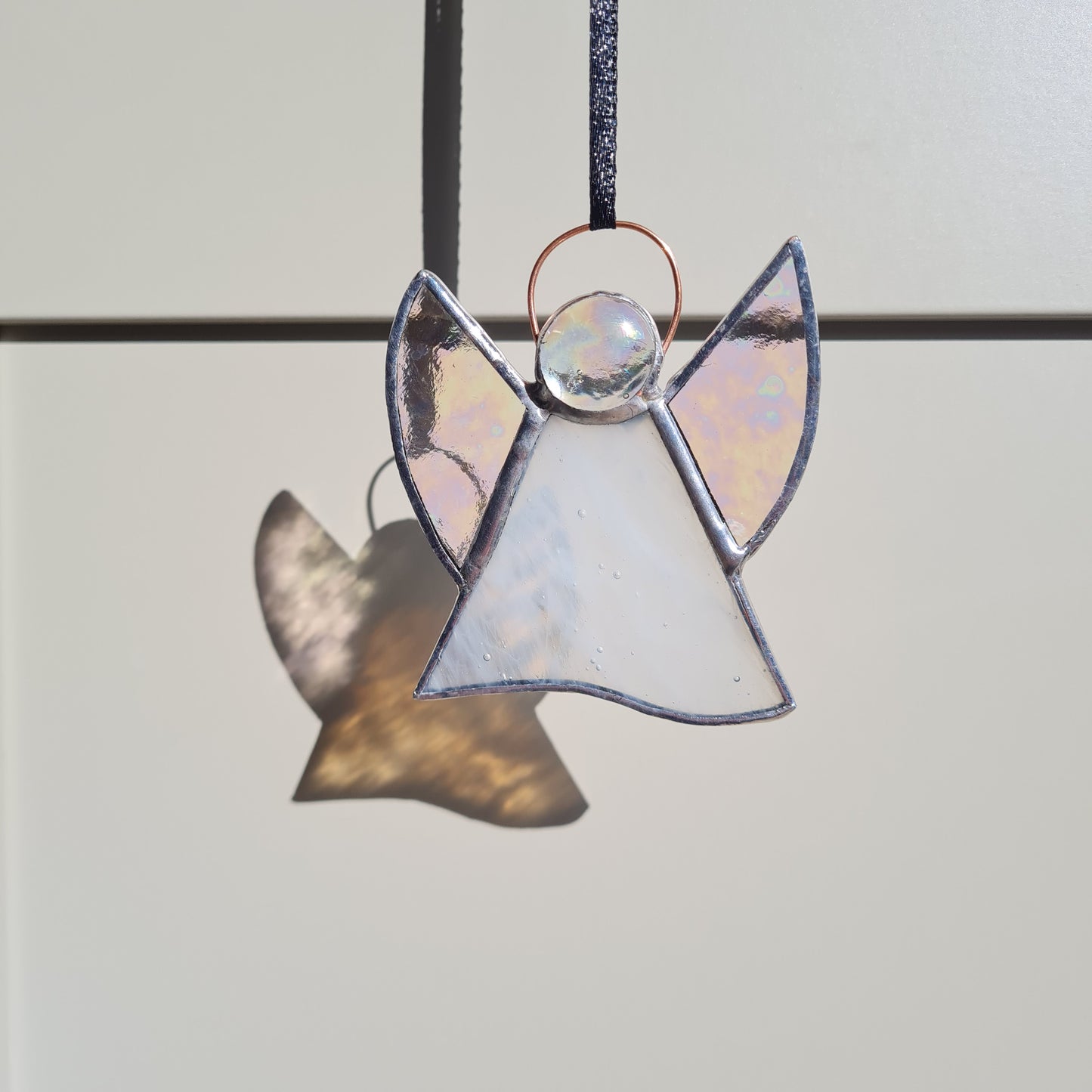 made from white and clear stained glass, the angel has wings and a copper wire halo