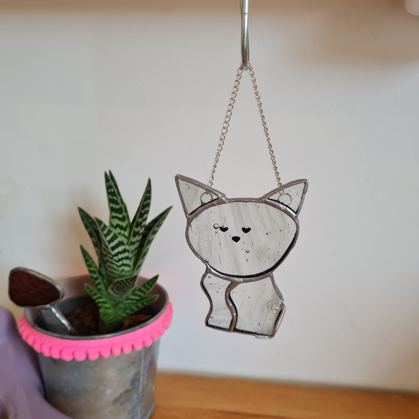 a small cat made from grey wispty stained glass. the cat has a curly wire ail and hangs on a chain.