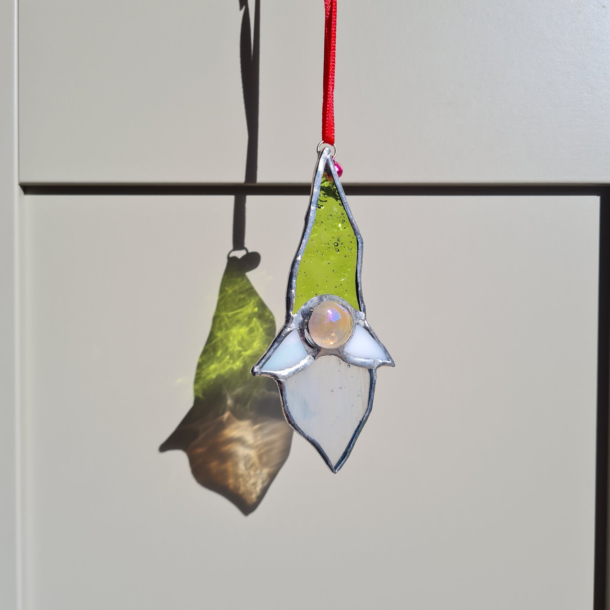 A stained glass gonk with  a lime green pointy hat, big glass nugget nose and a white beard and moustache