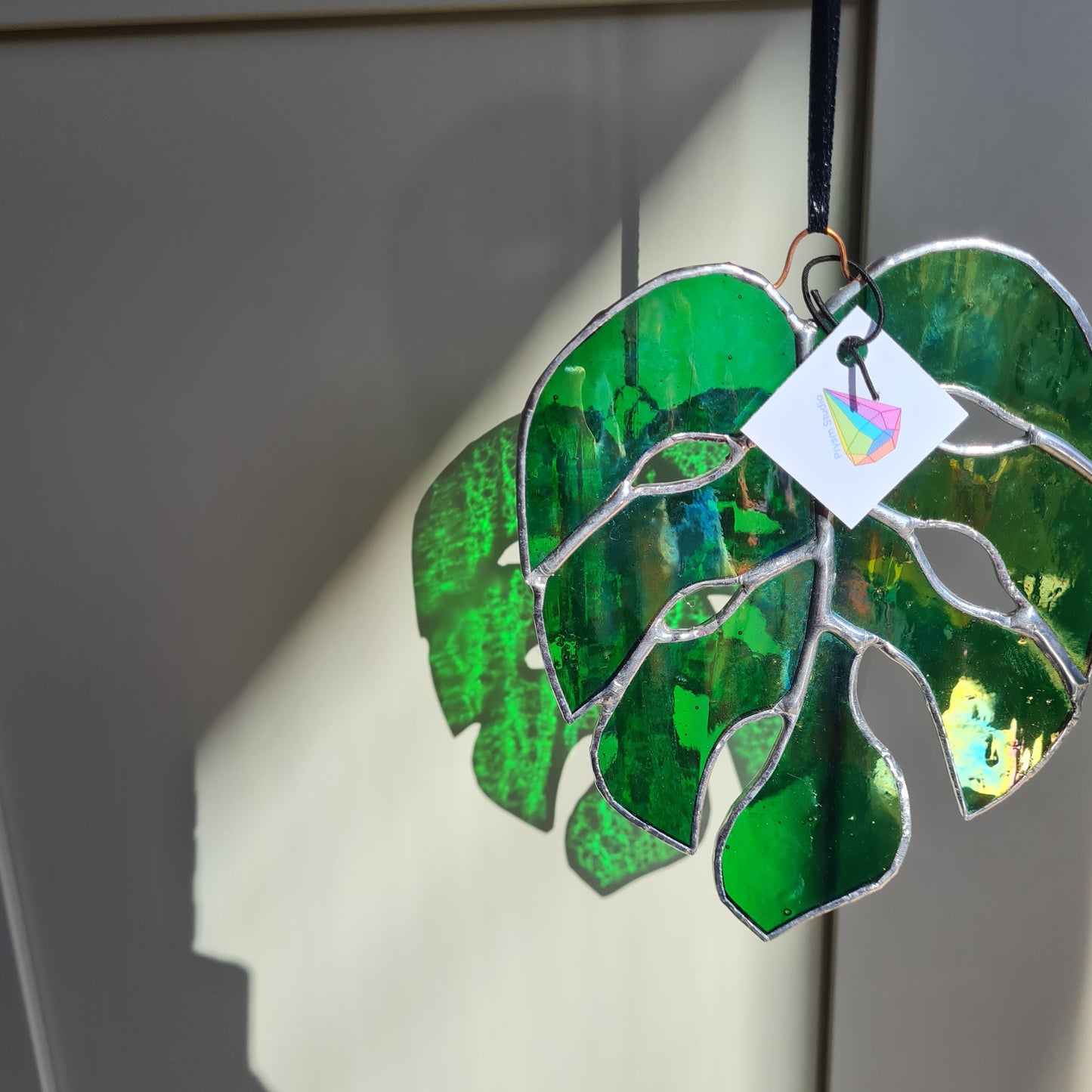 Iridescent green staines glass monstera leaf. hangin from a copper wire.