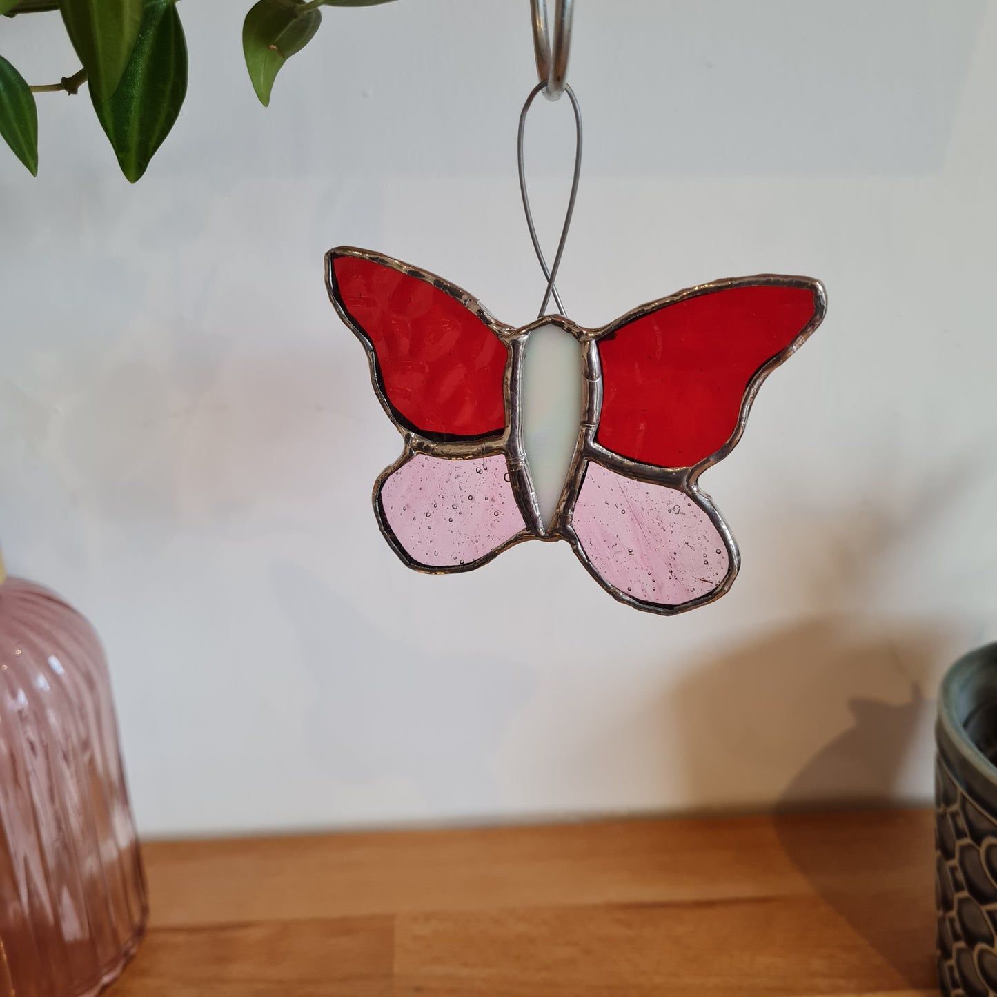 stained glass butterfly, top winds are red glass and bottom wings are pink. the body of the butterfly is white glass and there is wire coming out the top to make a hanging loop.